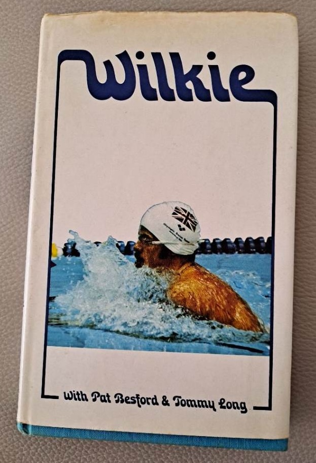 Dust jacket of Wilkie, showing David Wilkie swimming breaststroke in a white cap bearing the Union Flag